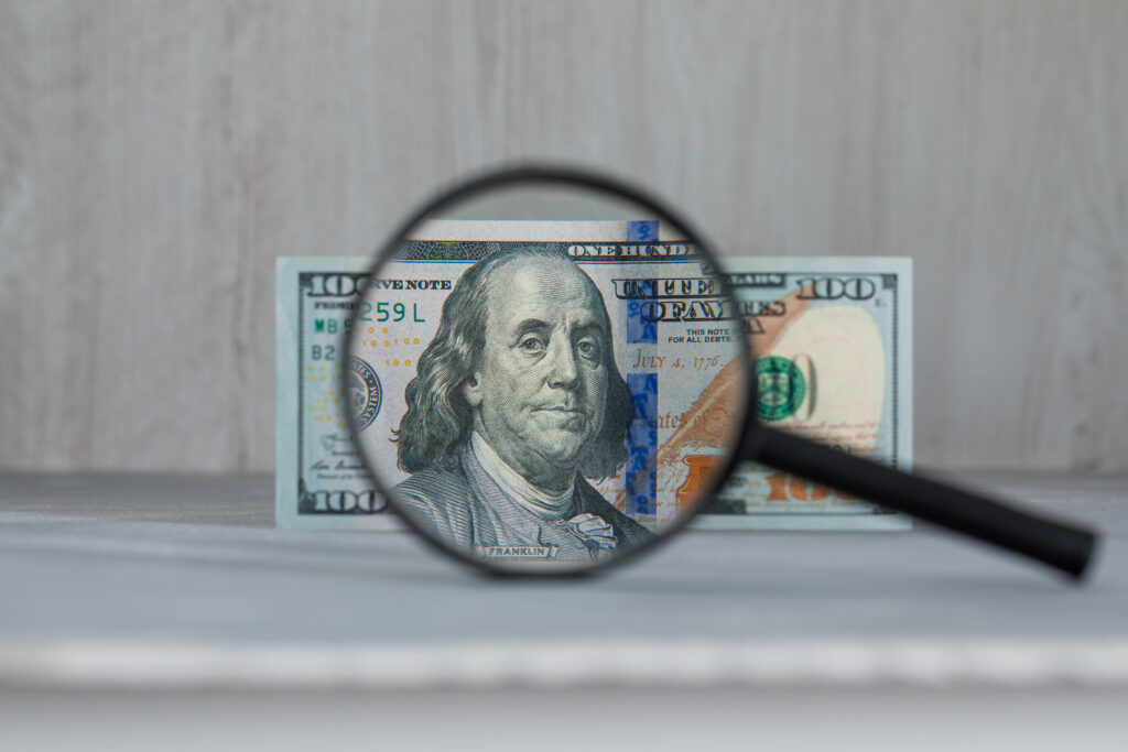 Business and monetary concept with magnifying glass over dollar banknote on grey and wooden background side view.